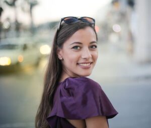 Cheerful woman in a purple top smiles at the camera on a bustling city street.